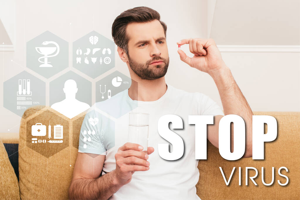 Homme réfléchi tenant pilule et verre d'eau sur le canapé à la maison, arrêter illustration de virus - Photo, image