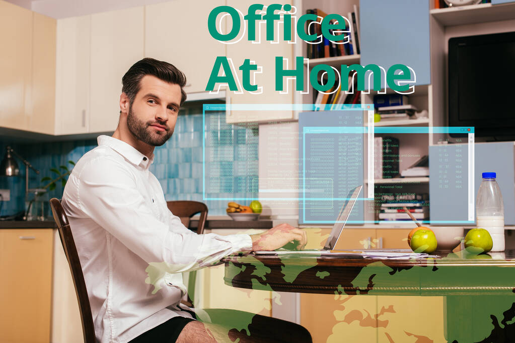 Вид сбоку на красивого фрилансера в рубашке и трусиках, смотрящего на камеру рядом с ноутбуком и завтраком на кухонном столе, домашняя иллюстрация офиса
 - Фото, изображение
