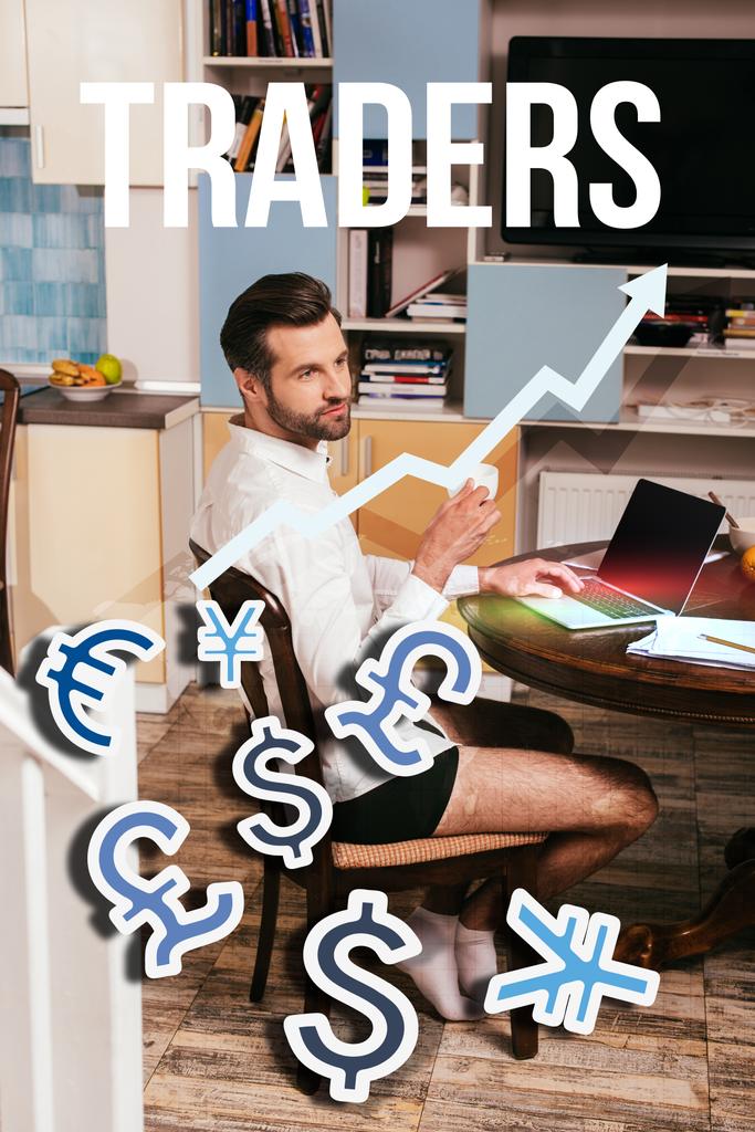Selective focus of handsome man in shirt and panties using laptop and holding cup in living room, traders illustration - Photo, Image