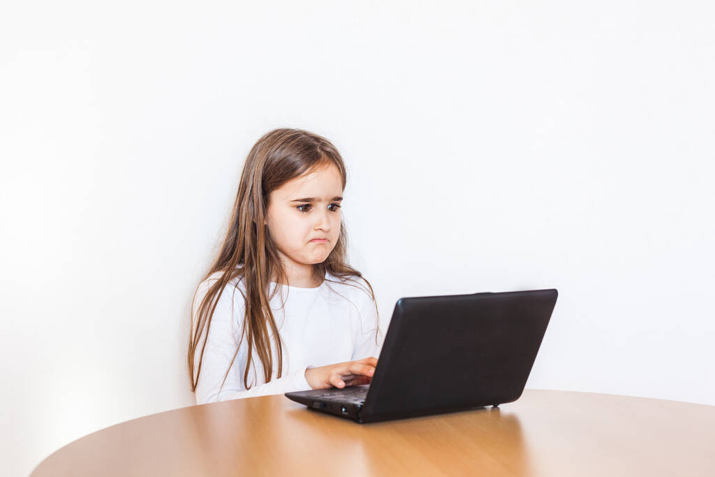 Uma menina da escola senta-se em uma mesa em casa e faz aulas através da Internet, estudando remotamente, gadgets, computador, escola, casa
 - Foto, Imagem