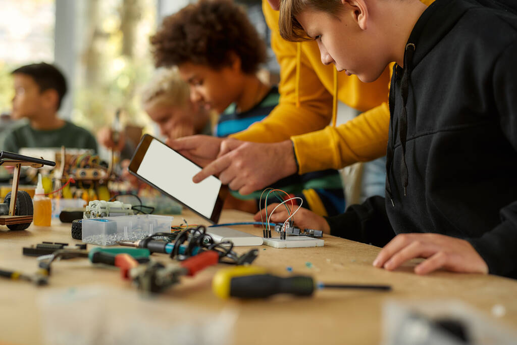 Fikirlerimizi paylaşıyoruz. Kök robotik dersinde kablo takımıyla çalışan genç teknisyenlerin görüntüsü. Erkek öğretmen onlara yardım ediyor, tavsiye veriyor, tablet bilgisayar kullanıyor. Çocuklar için icatlar ve yaratıcılık - Fotoğraf, Görsel