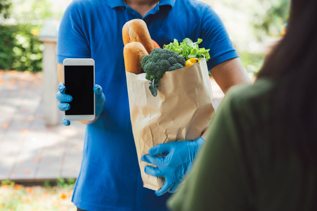 Zusteller in blauem Hemd übergibt dem Kunden das Telefon und bestätigt den Erhalt des Produktes. Lieferservice während covid19.New normal. - Foto, Bild