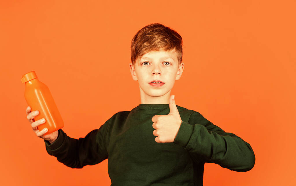 あなたはこの製品が好きです。小さな男の子はジュースオレンジの背景のために親指を表示します。ビタミンドリンク。飲料品。有機物入りボトル。健康的な飲酒習慣。製品の普及 - 写真・画像