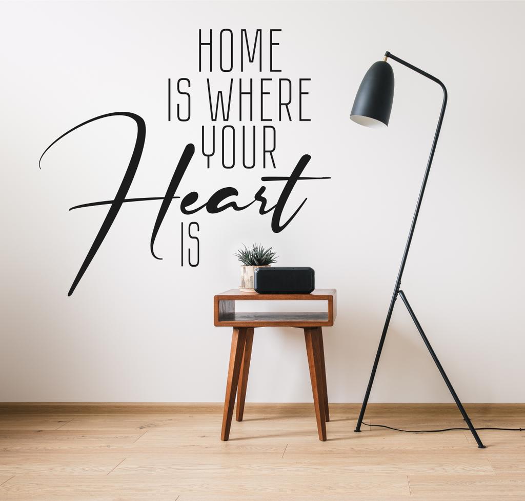 lampada da terra e tavolino in legno con pianta vicino orologio con schermo bianco e la casa è dove il vostro cuore è lettering
  - Foto, immagini
