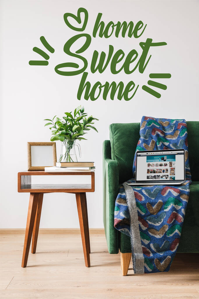 KYIV, UKRAINE - APRIL 14, 2020: home sweet home lettering near green sofa, blanket, laptop with amazon website and wooden coffee table  - Photo, Image