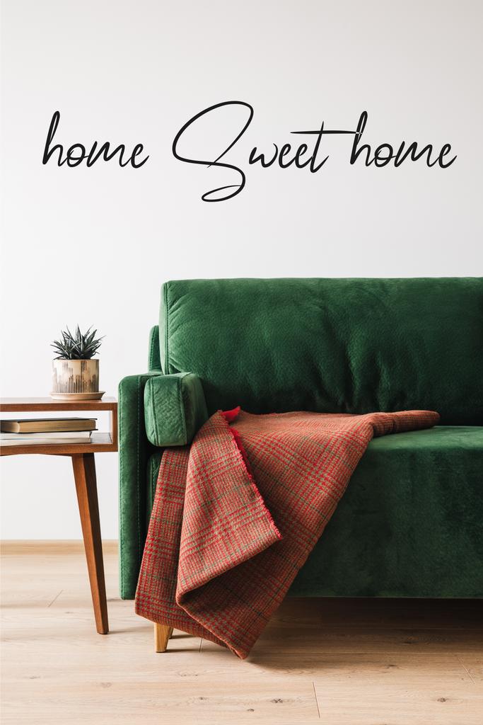zielona sofa, koc i drewniany stolik kawowy z roślinami i książkami w pobliżu domu słodki napis  - Zdjęcie, obraz