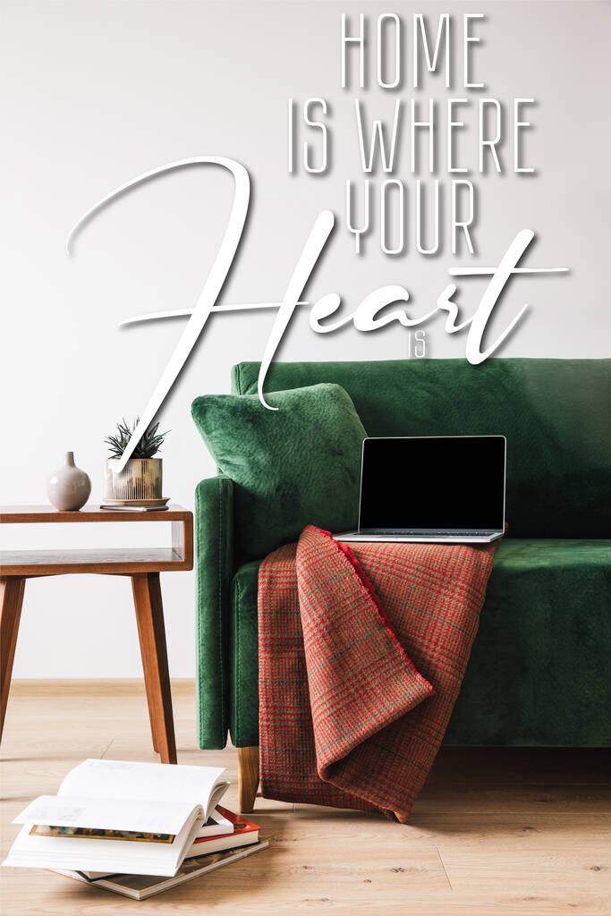 groene bank met deken en laptop in de buurt van houten salontafel en huis is waar uw hart is belettering - Foto, afbeelding