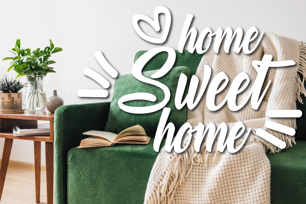 grünes Sofa, Kissen, Buch und Decke in der Nähe des Holztisches mit Pflanzen und hausgemachten süßen Schriftzügen  - Foto, Bild
