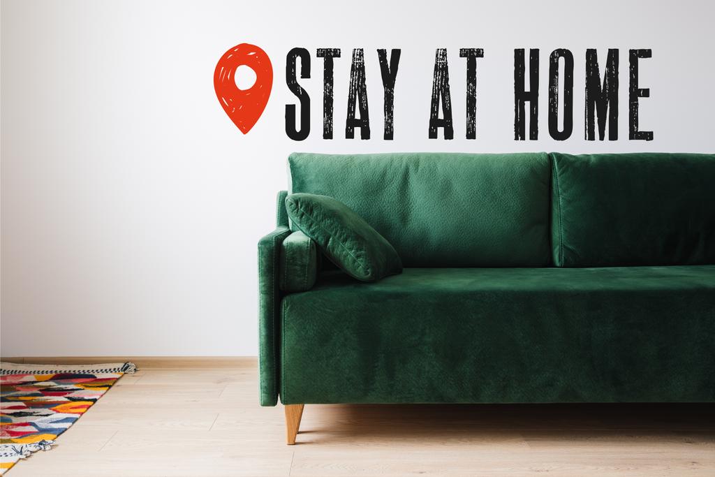 zielona sofa z poduszką w pobliżu kolorowego dywanu i pobyt w domu liternictwo  - Zdjęcie, obraz