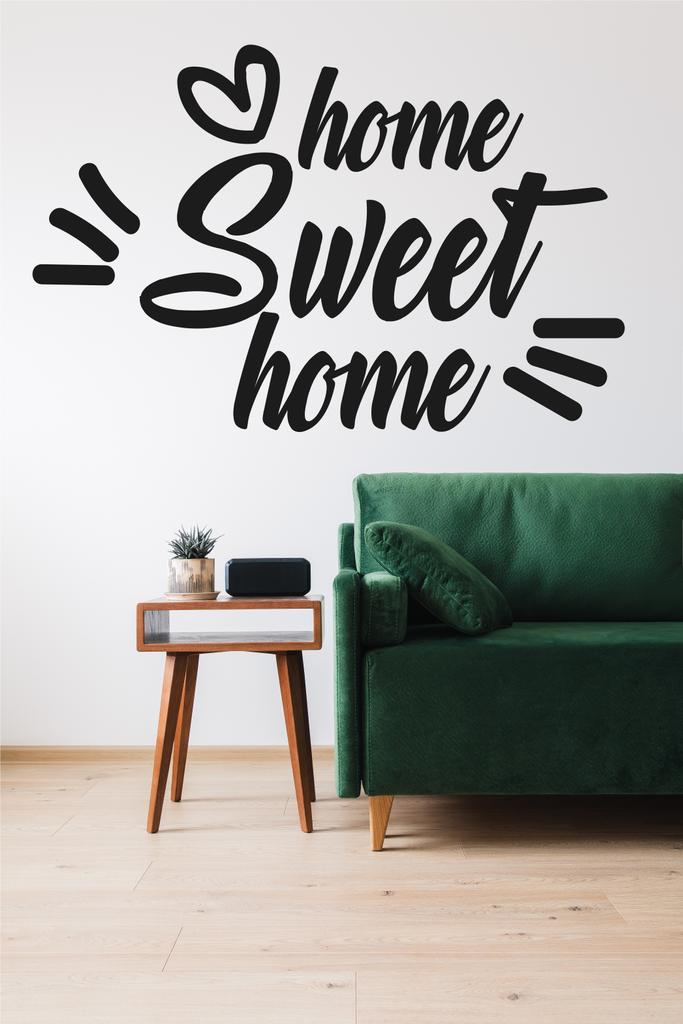 modernes grünes Sofa, Kissen, Holztisch mit Pflanze und Wecker in der Nähe von zu Hause Sweet Home Schriftzug  - Foto, Bild