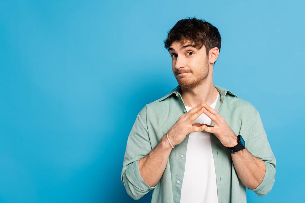 skeptický mladý muž stojící se spojenými prsty na modré - Fotografie, Obrázek