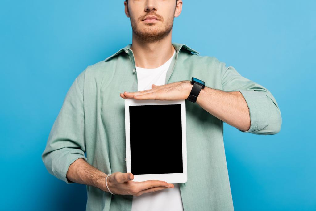 oříznutý pohled na mladého muže zobrazujícího digitální tablet s prázdnou obrazovkou na modré - Fotografie, Obrázek