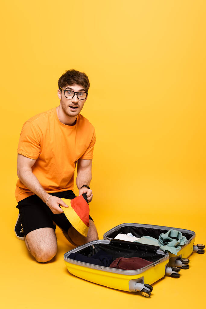 surprised male tourist packing luggage for summer vacation on yellow  - Photo, Image