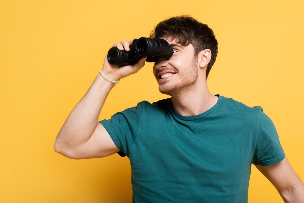 handsome smiling man looking through binoculars on yellow - Photo, Image