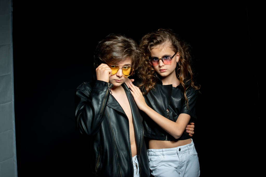 preteen junge und mädchen in lederbekleidung posieren im studio auf dunklem hintergrund - Foto, Bild