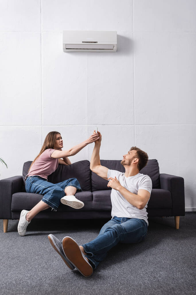 pareja enojada con mando a distancia en casa con aire acondicionado roto
  - Foto, Imagen