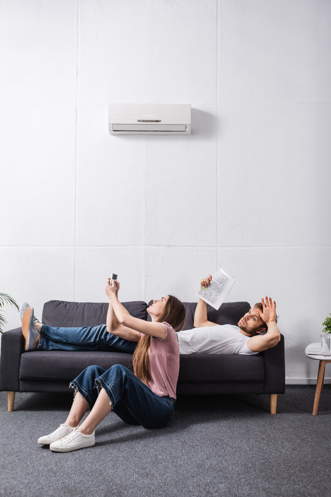 pareja enojada que sufre de calor mientras está sentada en casa con el aire acondicionado roto
  - Foto, Imagen