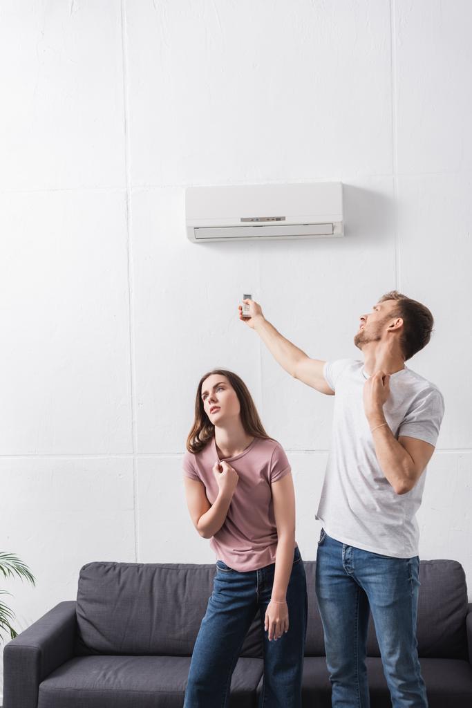 uitgeput koppel met afstandsbediening last van warmte thuis met gebroken airconditioner  - Foto, afbeelding