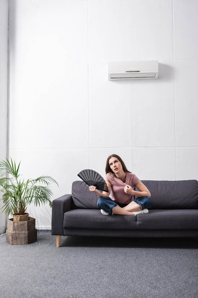 overstuur jonge vrouw die last heeft van warmte en het gebruik van de hand ventilator thuis met gebroken conditioner - Foto, afbeelding