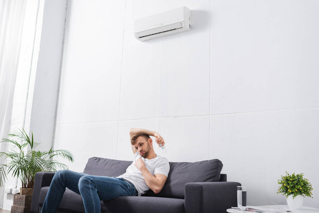 trieste man voelt zich ongemakkelijk met gebroken airconditioner thuis tijdens de zomer warmte  - Foto, afbeelding