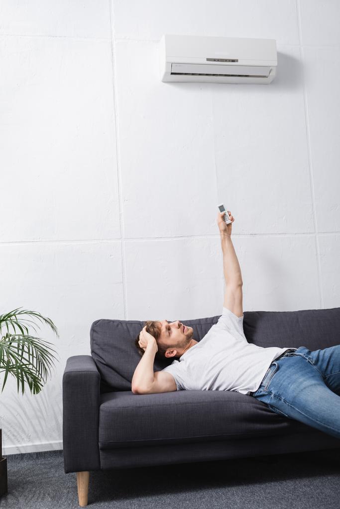 σύγχυση άνθρωπος κρατώντας τηλεχειριστήριο και πάσχουν από θερμότητα με σπασμένο κλιματιστικό στο σπίτι  - Φωτογραφία, εικόνα