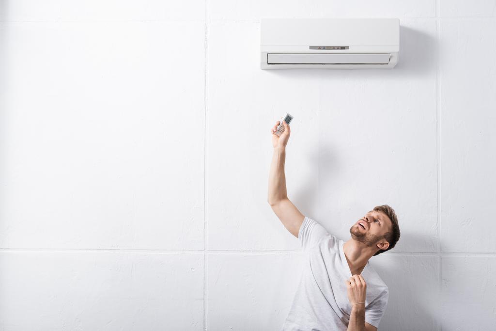 смущенный человек держит пульт дистанционного управления и страдает от жары со сломанным кондиционером воздуха дома
  - Фото, изображение