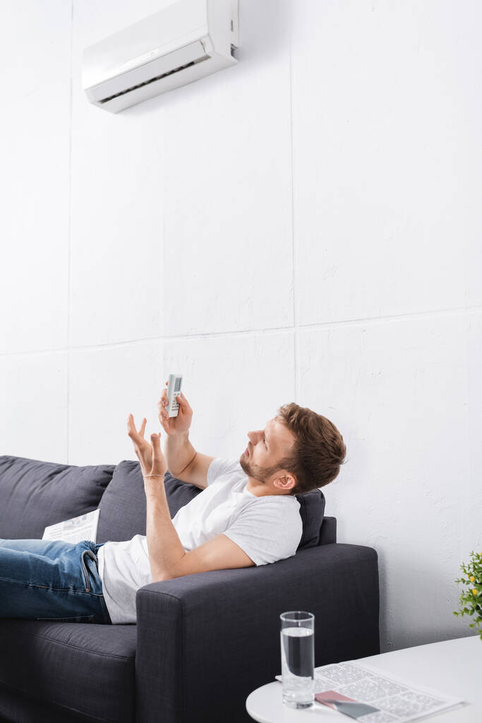 homem confuso tentando ligar ar condicionado com controle remoto em casa
  - Foto, Imagem