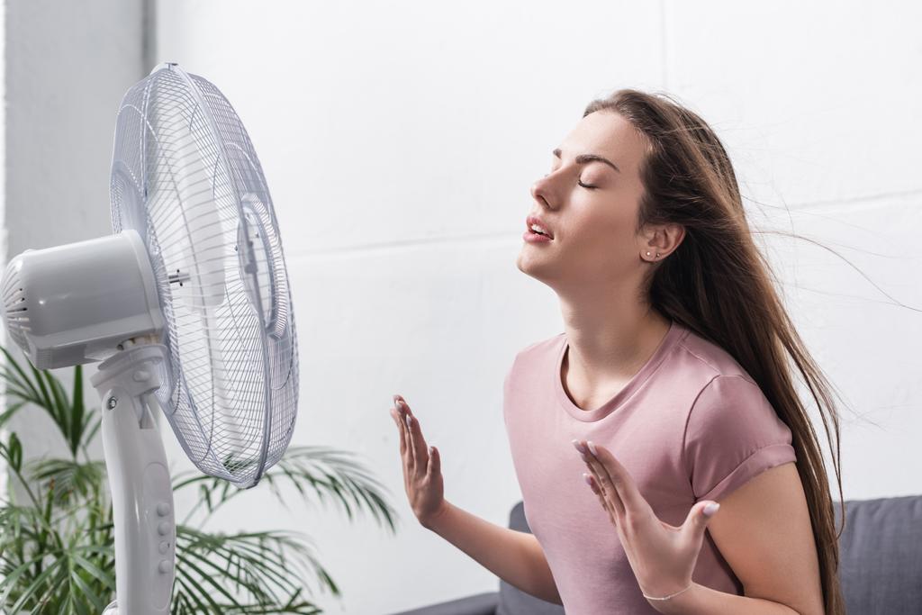 красивая девушка чувствует себя комфортно с электрическим вентилятором во время летней жары
 - Фото, изображение