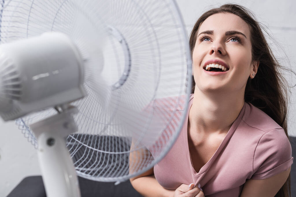 donna eccitata sentirsi a proprio agio con ventilatore elettrico a casa durante il caldo estivo - Foto, immagini