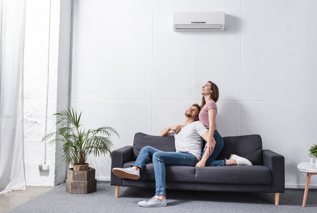 glimlachende vriendin en vriendje knuffelen thuis met airconditioner - Foto, afbeelding