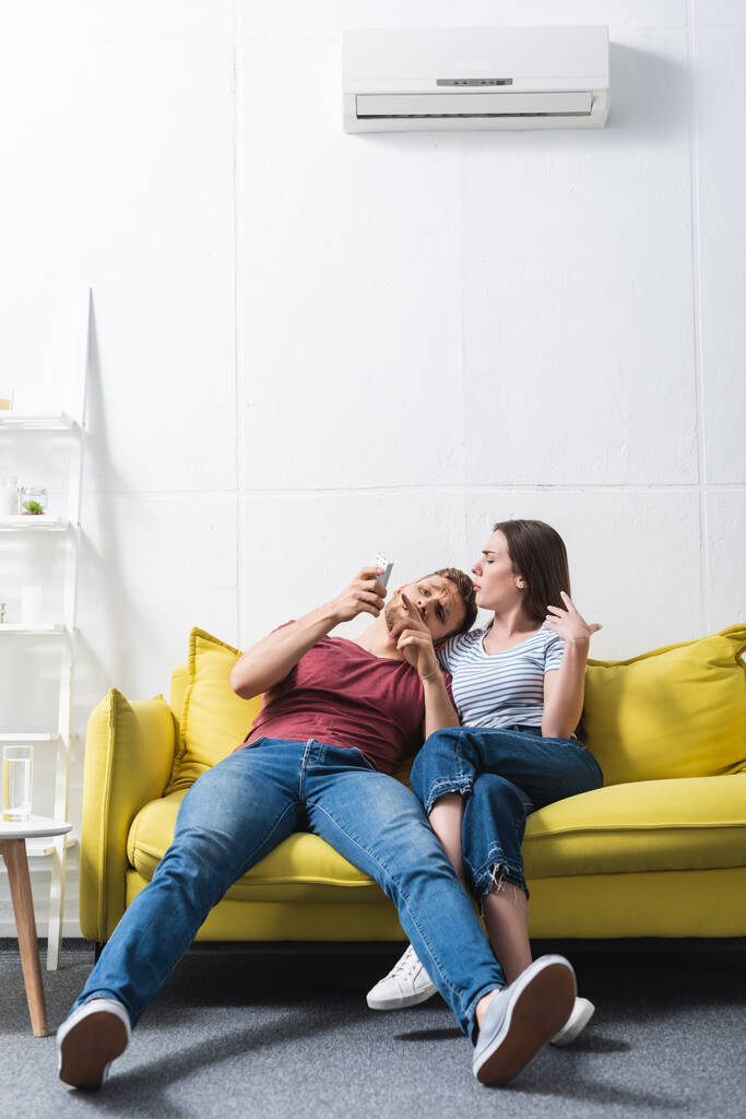 jeune couple confus avec télécommande souffrant de chaleur à la maison avec climatiseur cassé  - Photo, image