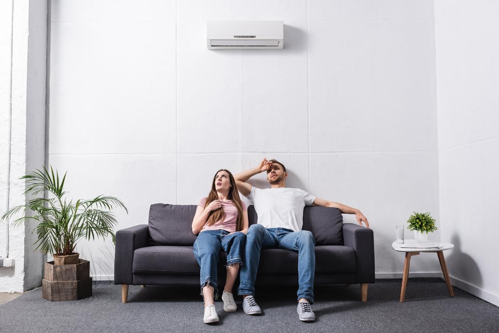joven pareja triste que sufre de calor mientras está sentado en casa con el aire acondicionado roto
  - Foto, Imagen