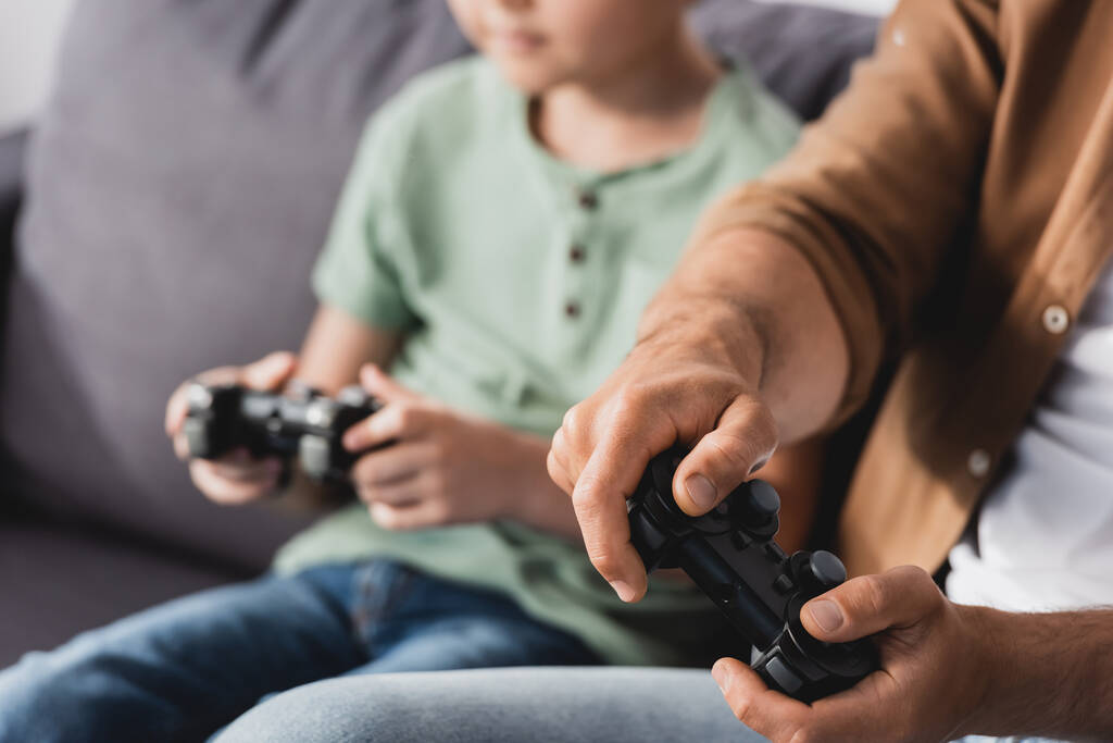 KYIV, UKRAINE - JUNE 9, 2020: cropped view of father and son playing video game with joysticks, selective focus - Photo, Image