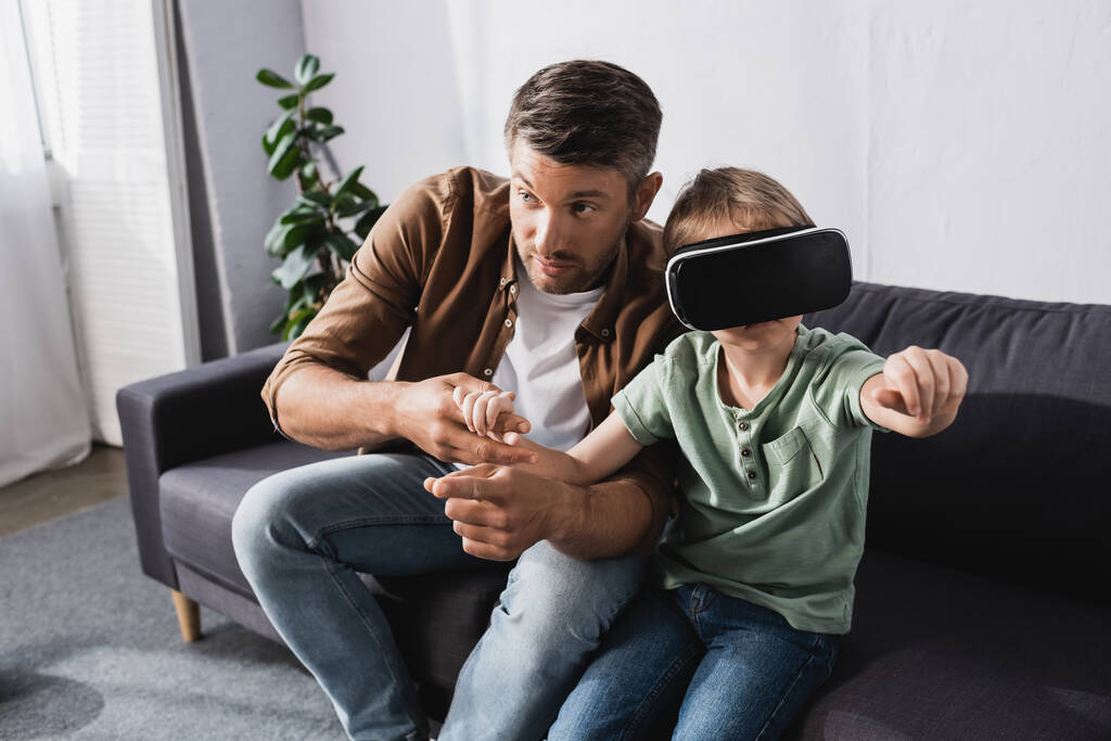 father touching hands of son gesturing while using vr headset - Photo, Image