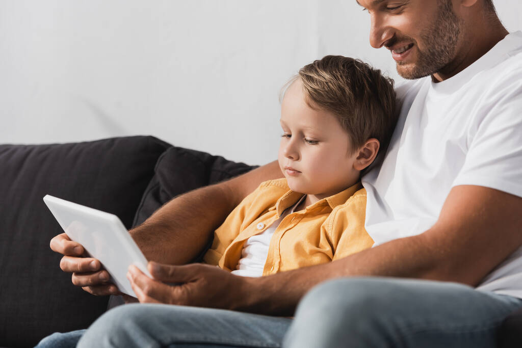 smiling father with adorable son using digital tablet together while sitting on sofa - Photo, Image