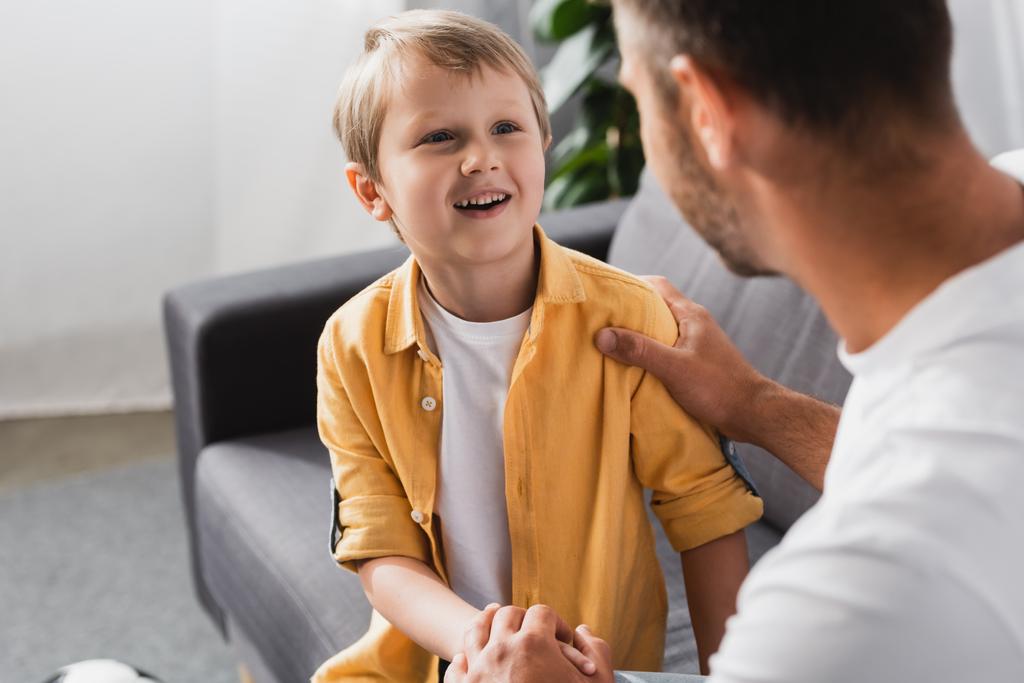 selektiver Fokus des Vaters, der Schulter und Hand des lächelnden Sohnes berührt, während er zu Hause mit ihm spricht - Foto, Bild