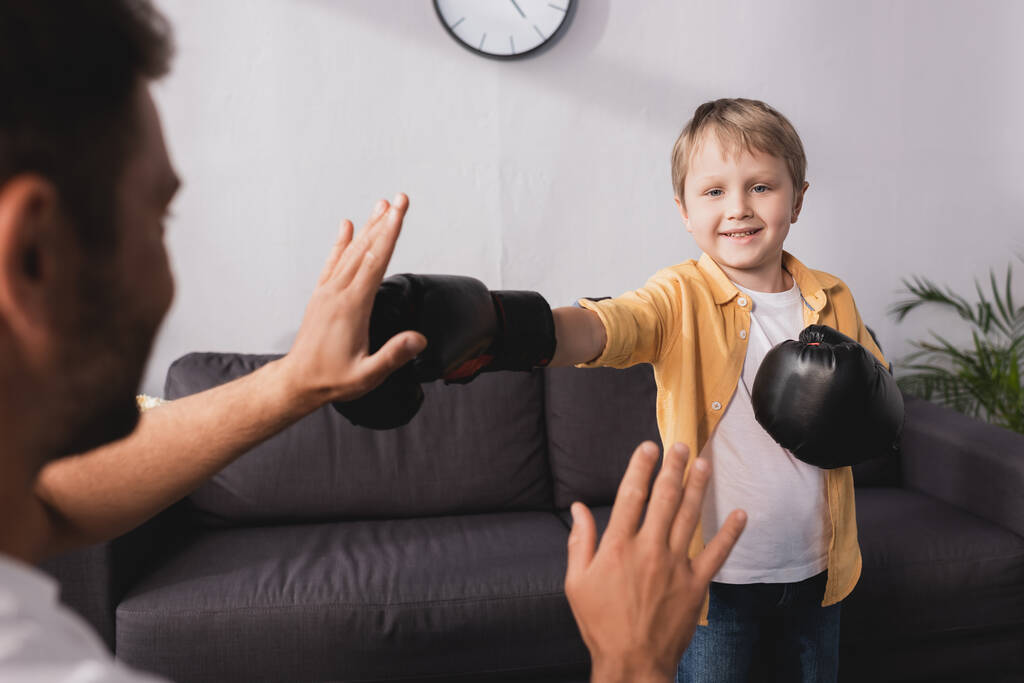 επιλεκτική εστίαση του χαμογελαστού αγοριού στην πυγμαχία γάντια αγωνίζονται με τον πατέρα - Φωτογραφία, εικόνα