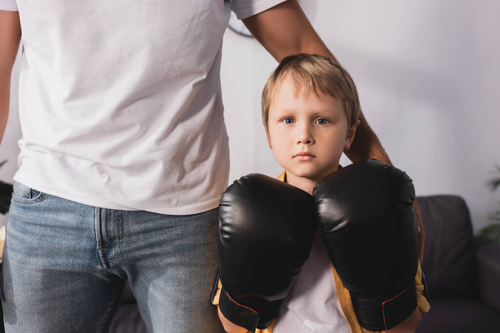 обрізаний вид батька торкається плеча милого серйозного сина в боксерських рукавичках
 - Фото, зображення