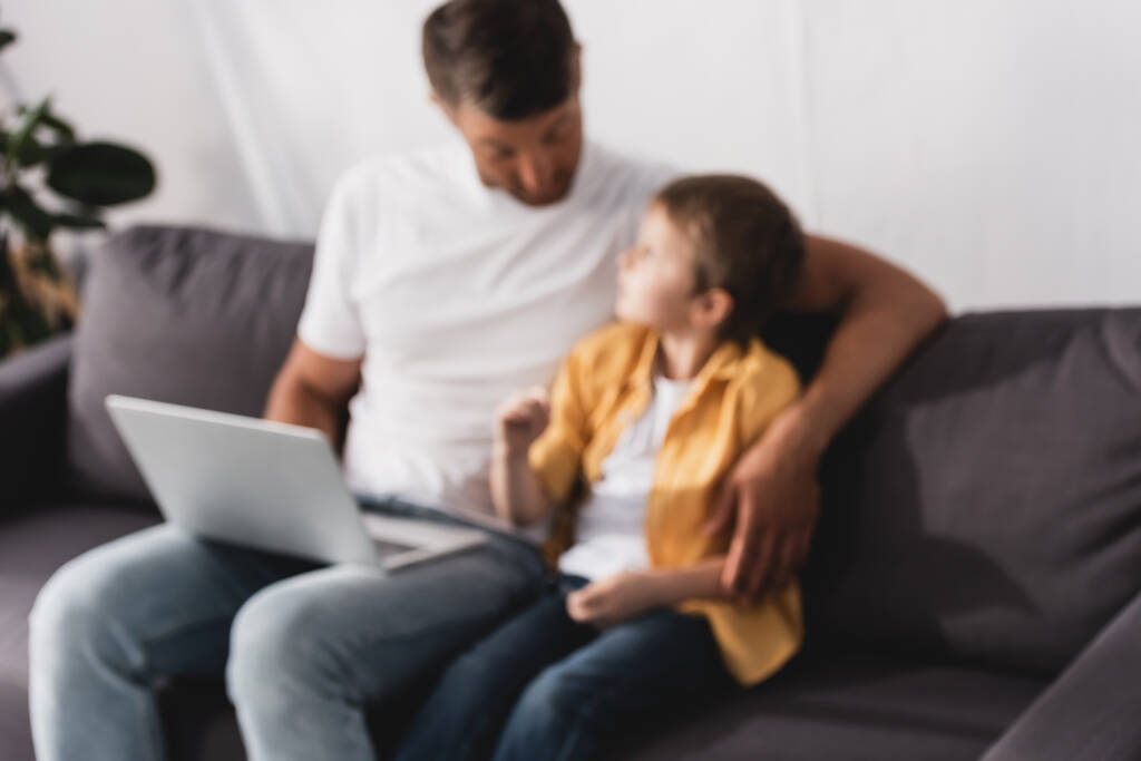 selektivní zaměření otce a syna sedí na pohovce, mluví a pomocí notebooku - Fotografie, Obrázek
