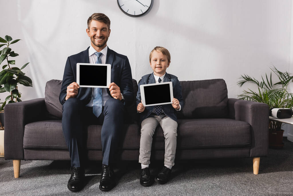 χαρούμενος επιχειρηματίας και γιος σε επίσημη φθορά που δείχνει ψηφιακές ταμπλέτες με λευκή οθόνη και κοιτάζοντας την κάμερα - Φωτογραφία, εικόνα