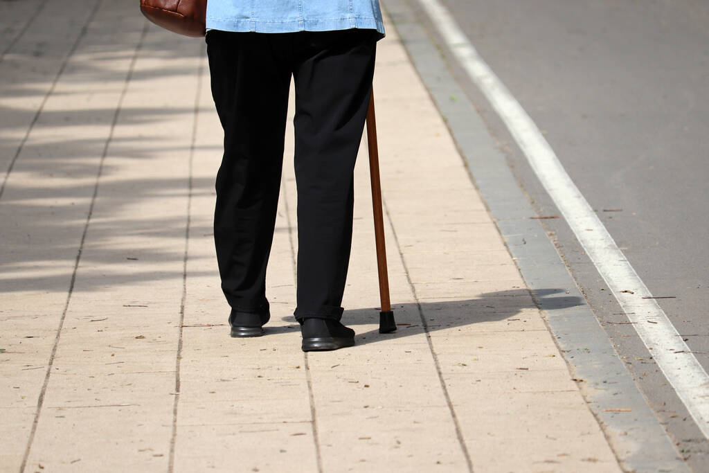 Женщина ходит с тростью на улице, женские ноги на тротуаре. Концепция инвалидности, хромота, заболевания позвоночника, пожилые люди
 - Фото, изображение
