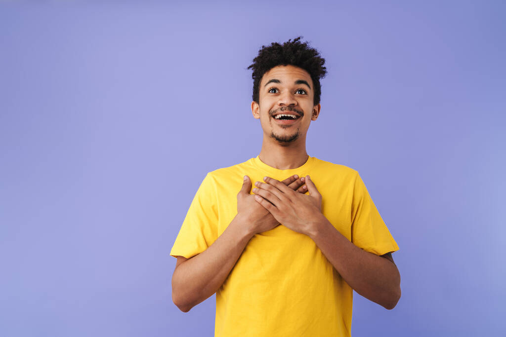 興奮したアフリカ系アメリカ人の男の写真手で笑顔胸の上に紫色の背景に隔離 - 写真・画像