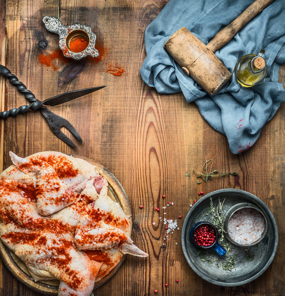 Whole chicken flattened out with meat hammer, spices and kitchen tools on wooden rustic background, cooking preparation , top view, frame. Chicken Tabaka traditional Georgian dish , Caucasian cuisine - Photo, Image