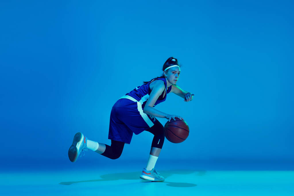 Mladý kavkazský ženský basketbalista izolovaný na modrém pozadí studia v neonovém světle - Fotografie, Obrázek