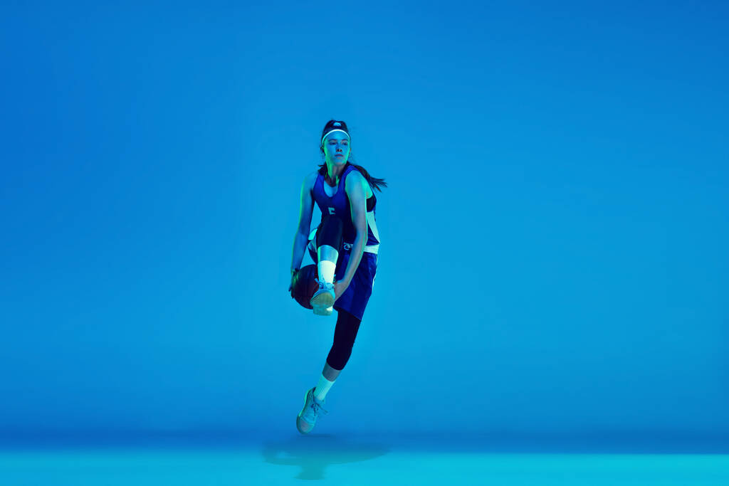Jeune joueuse de basket caucasienne isolée sur fond de studio bleu au néon - Photo, image