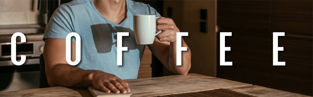 orientación panorámica del hombre sosteniendo taza cerca de libro y letras de café en casa
 - Foto, Imagen