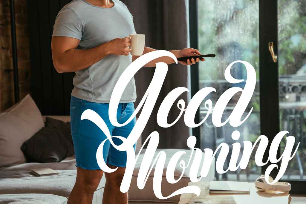 bijgesneden weergave van de mens met kopje koffie houden afstandsbediening in de buurt van goede ochtend belettering  - Foto, afbeelding