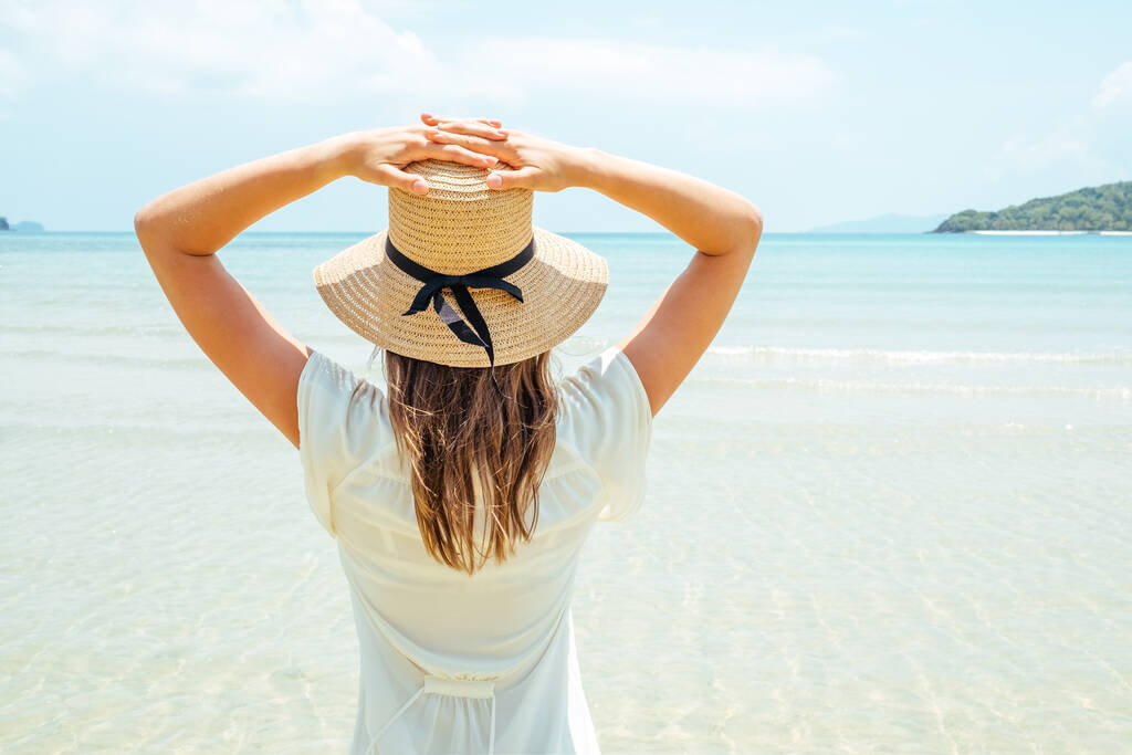 Nyári vakáción szalmakalapot viselő nő élvezi a kilátást az óceánra - Fotó, kép