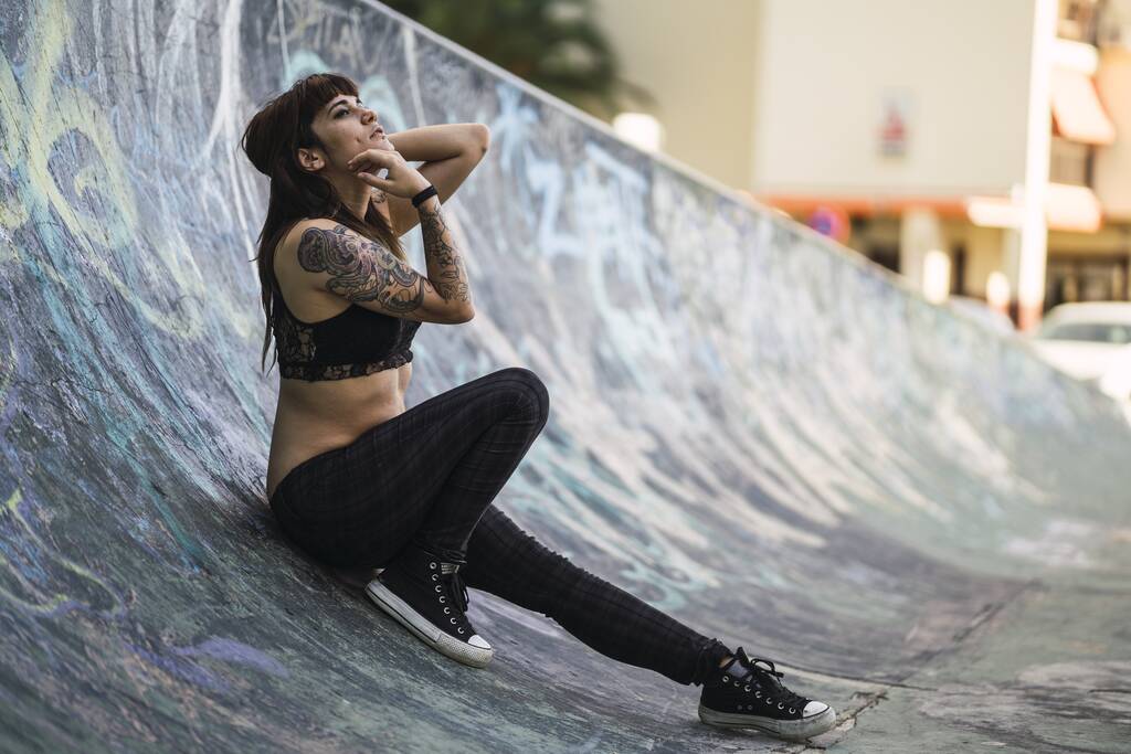 Uma jovem mulher branca atraente com tatuagens sentadas em uma rampa de patinação - Foto, Imagem