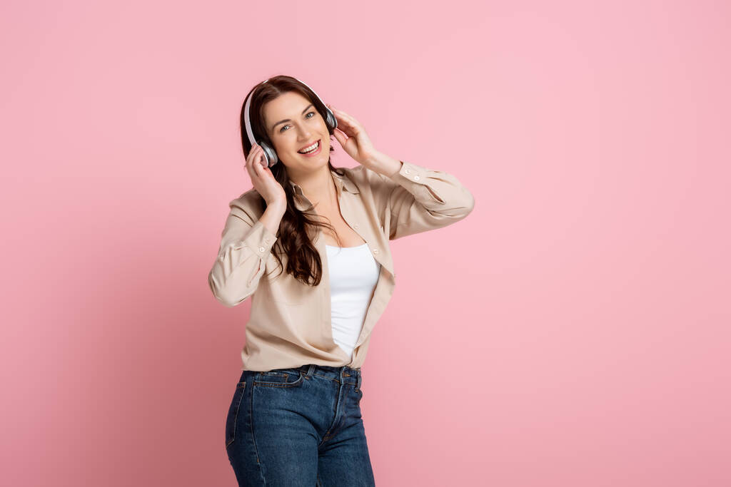 Mulher positiva ouvindo música em fones de ouvido no fundo rosa
 - Foto, Imagem